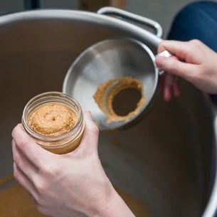 A person manually fills a nut butter jar. They are using a funnel.