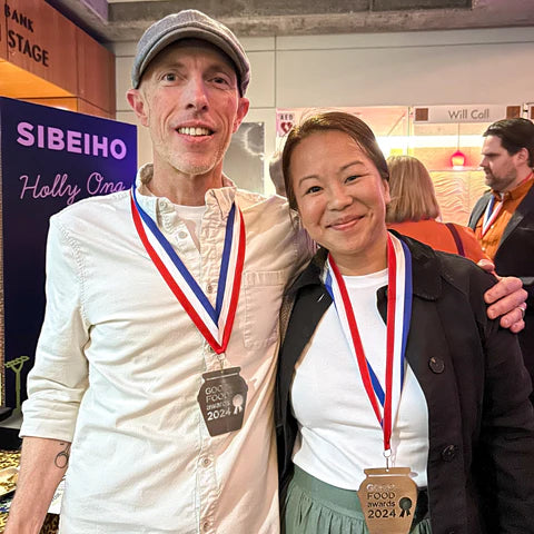 A tall man in a hat (Mark) stands with a shorter woman (a fellow GFA winner) in front of a crowd of people