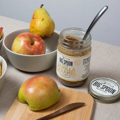 A jar of Vanilla Caramel Almond & Cashew Butter is open on a table with pears and apples.