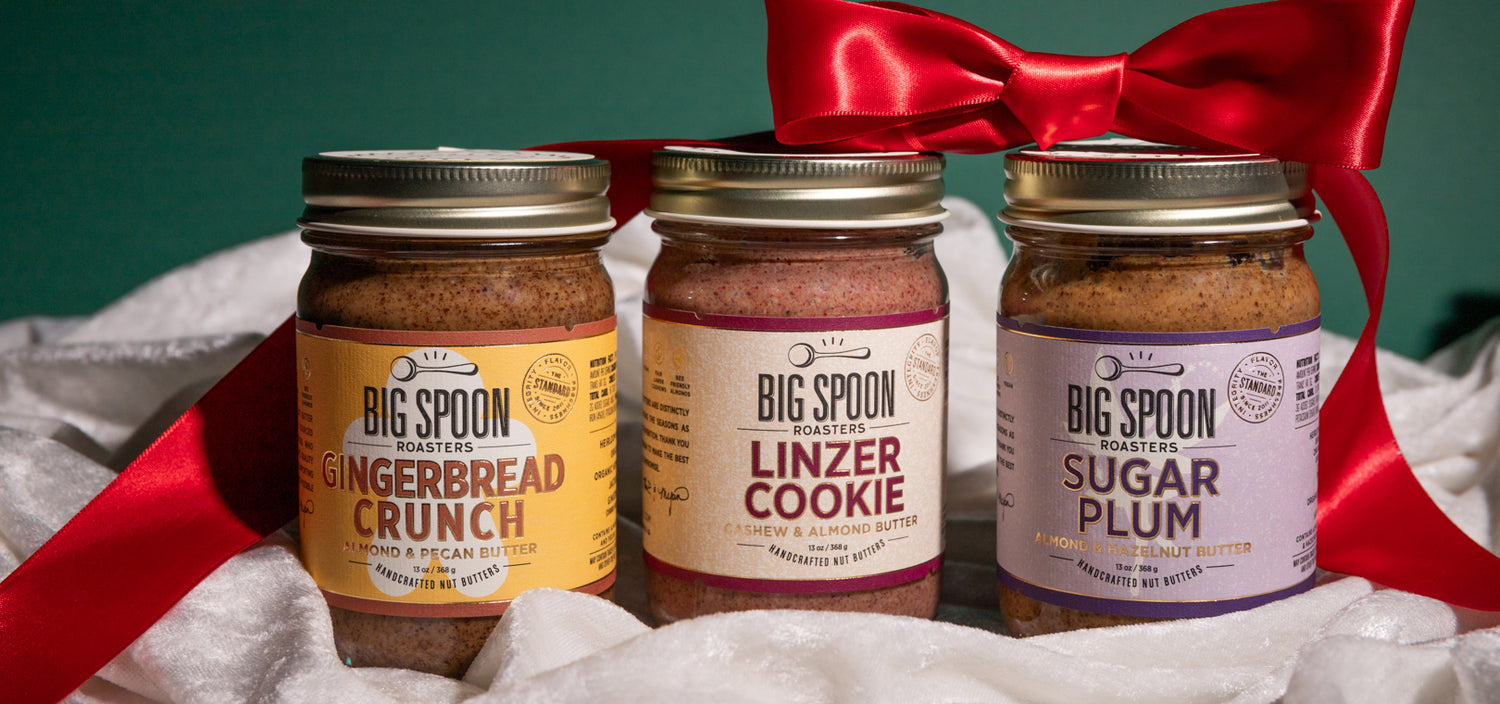 Three jars of Big Spoon Roasters nut butters with a red ribbon on a white fabric background.