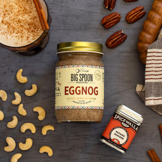 Jar of Eggnog nut butter surrounded by cashews, pecans, nutmeg, and eggnog