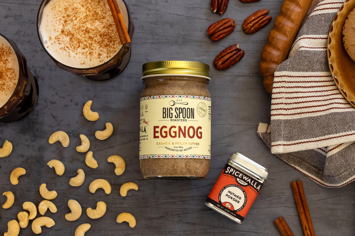 Jar of Eggnog nut butter surrounded by cashews, pecans, nutmeg, and eggnog