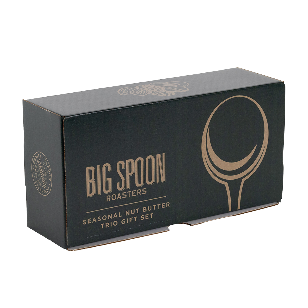 A dark green gift box for Big Spoon Roasters, featuring gold foil text that reads 'BIG SPOON ROASTERS' and 'SEASONAL NUT BUTTER TRIO GIFT SET', along with a large gold spoon graphic on the front, photographed on a white background.