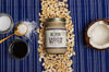 Jar of Big Spoon Cashew Butter surrounded by cashews, coconut, coconut nectar and oil, and salt on a blue striped background
