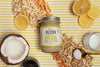Jar of Lemon Cookie Cashew Butter with lemon, coconut, cashews, salt, and coconut nectar/oil around it on a yellow striped background