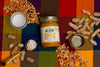 Jar of Big Spoon Peanut Butter surrounded by peanuts, coconut oil, honey, and salt on a colorful checkered background