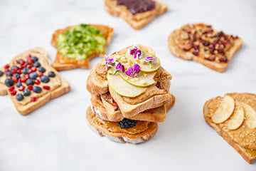 Slices of toast stacked with different nut butters and toppings on a white marbled surface