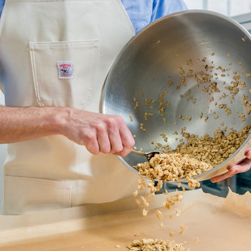 A hand uses a silver spoon to scrape oats out of a silver bowl onto a parchment lined sheet pan