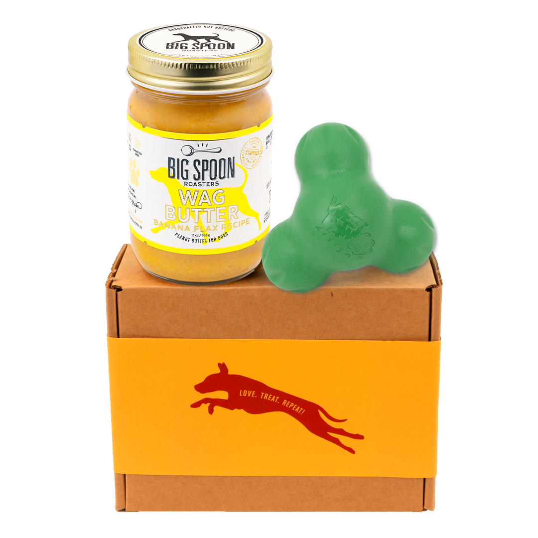 Jar of 'Big Spoon Roasters' Wag Butter on a box with a green West Paw Tux toy.