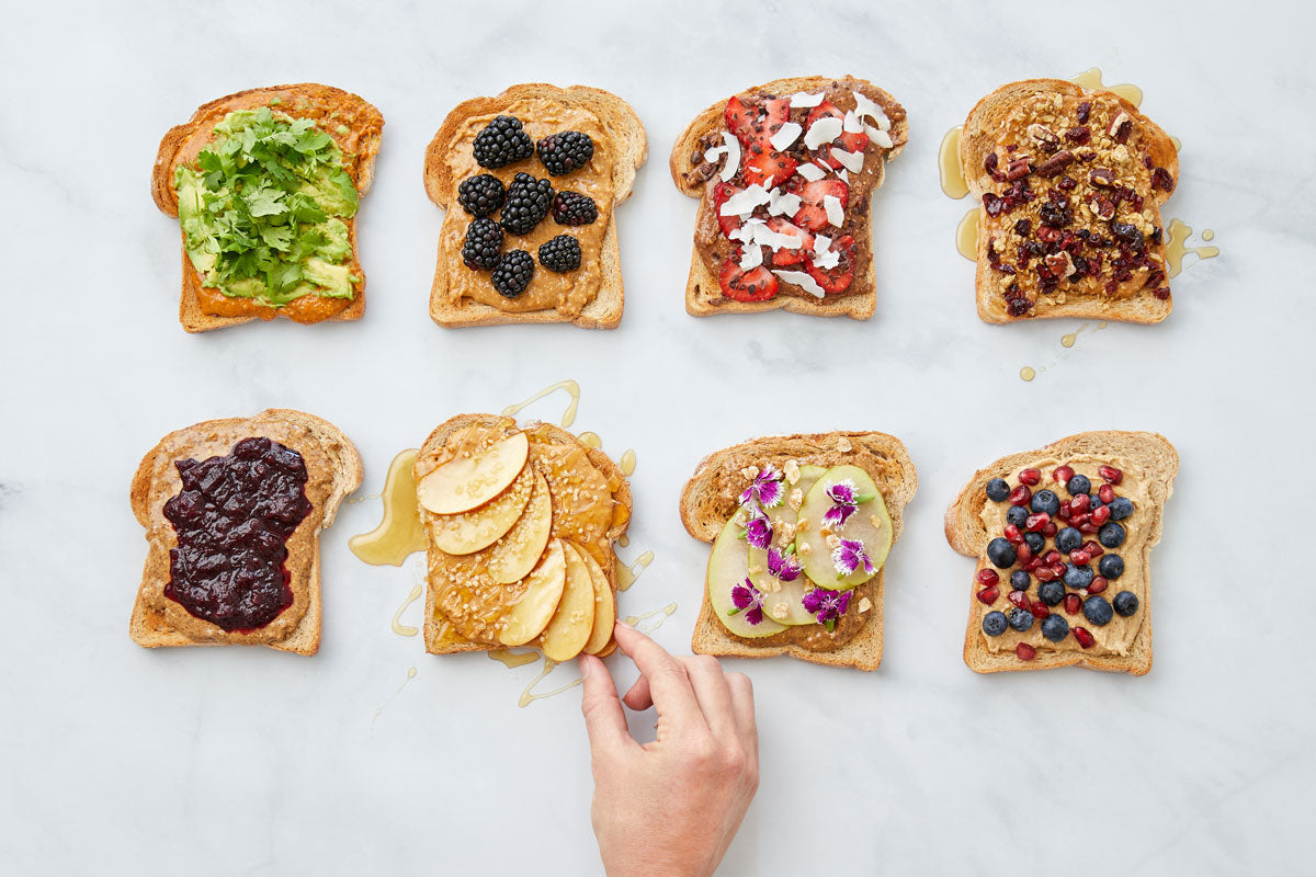 A hand reaches for a piece of toast, surrounded by several other pieces of toast with different variations of nut butter and toppings