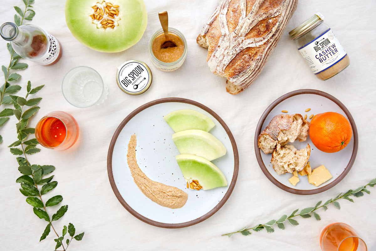 Tabletop spread featuring melon, citrus, plants, Cashew Butter with Coconut Nectar