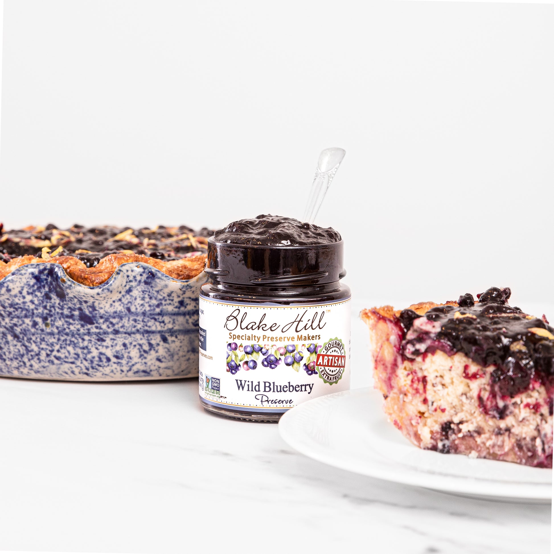 jar of Wild Blueberry Preserves, open surrounded by cheesecake