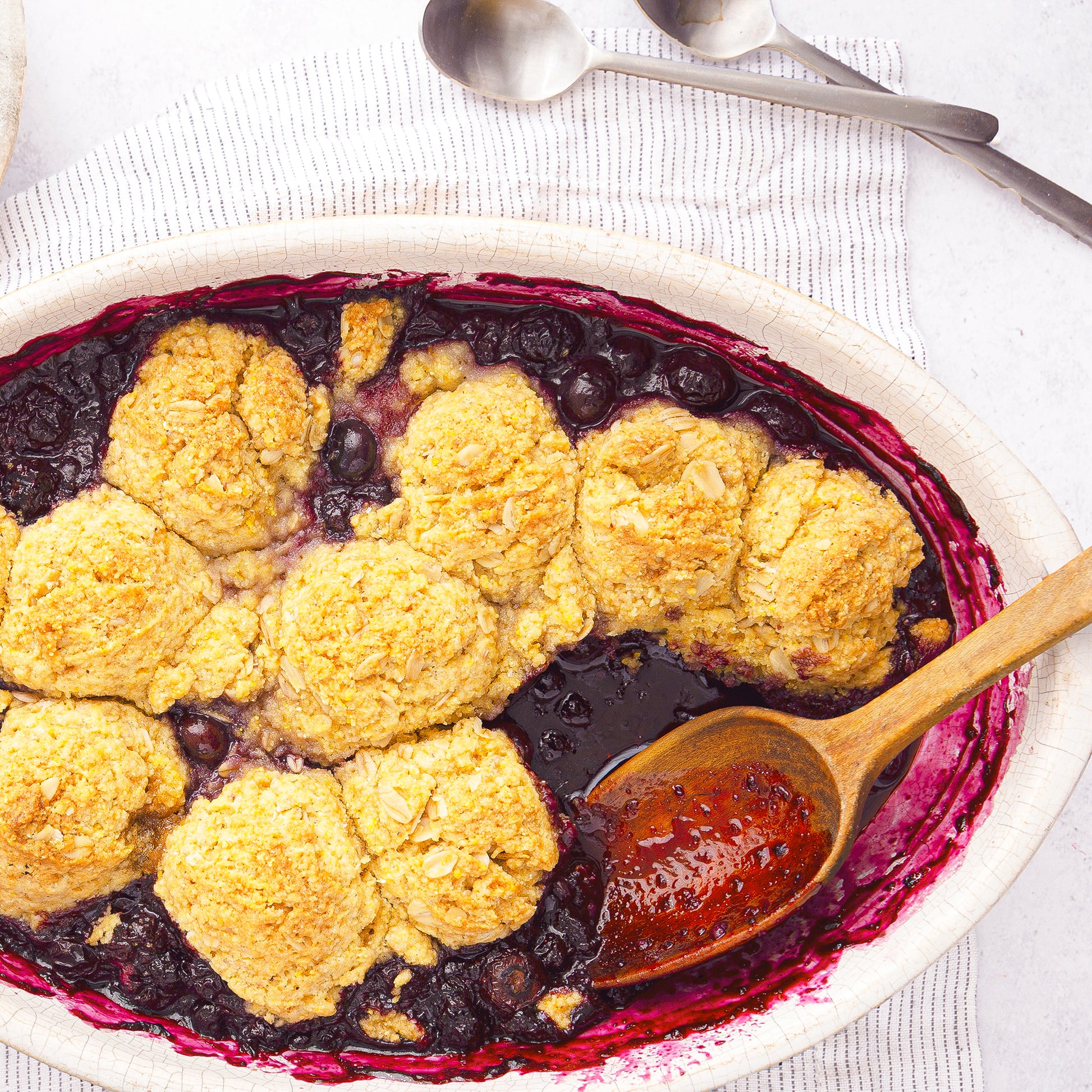 top-down image of a blueberry cobbler with a wooden spoon inside