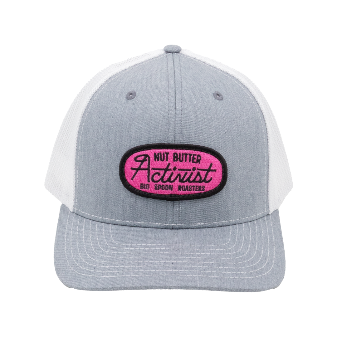 Light gray trucker hat with pink patch reading "NUT BUTTER ACTIVIST BIG SPOON ROASTERS"