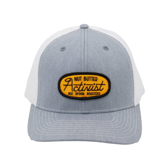 Light gray trucker hat with yellow patch reading "NUT BUTTER ACTIVIST BIG SPOON ROASTERS"