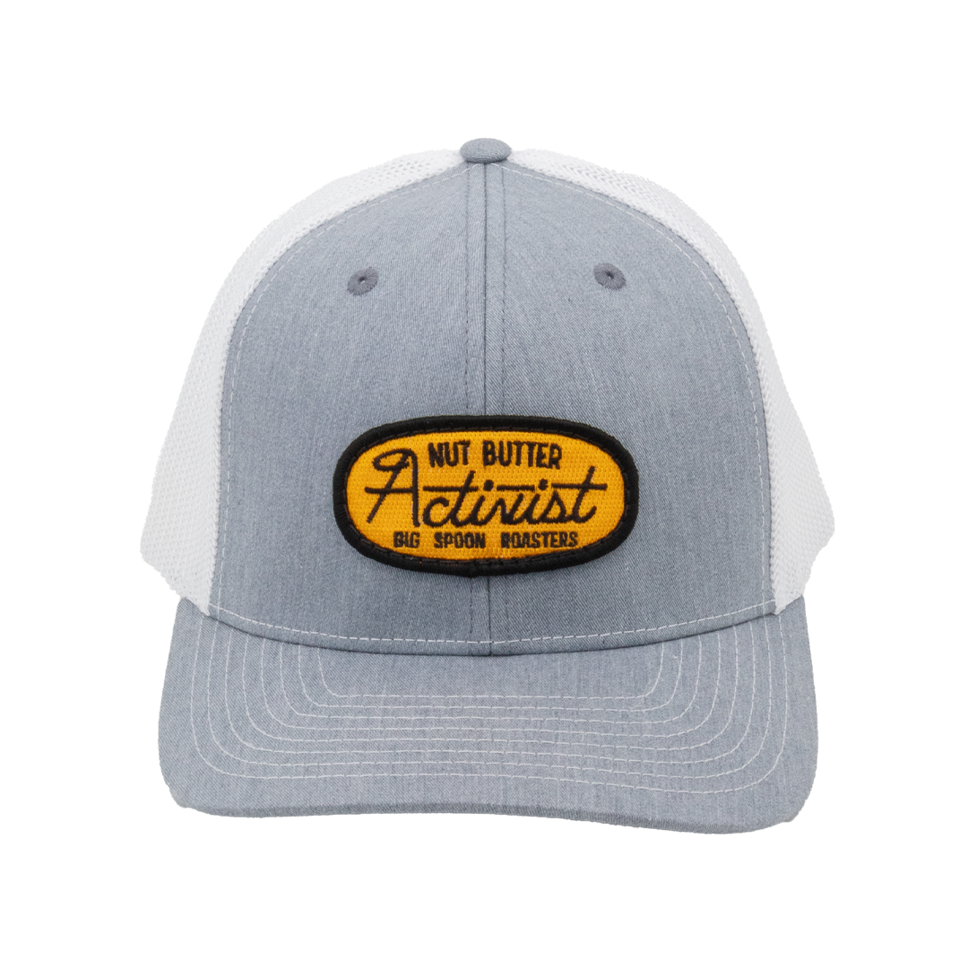 Light gray trucker hat with yellow patch reading "NUT BUTTER ACTIVIST BIG SPOON ROASTERS"