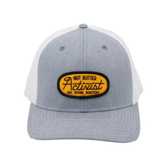 Light gray trucker hat with yellow patch reading "NUT BUTTER ACTIVIST BIG SPOON ROASTERS"