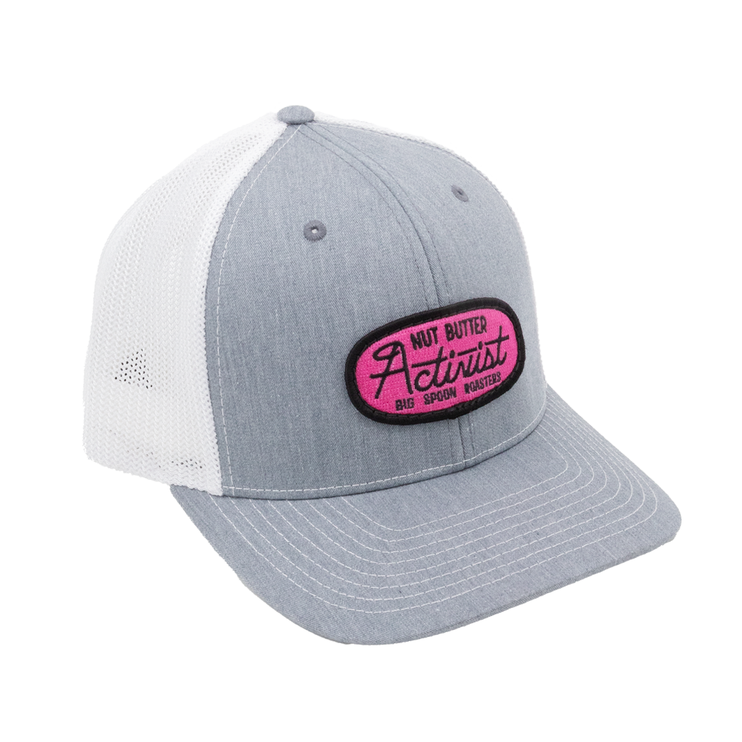 Light gray trucker hat with pink patch reading "NUT BUTTER ACTIVIST BIG SPOON ROASTERS"