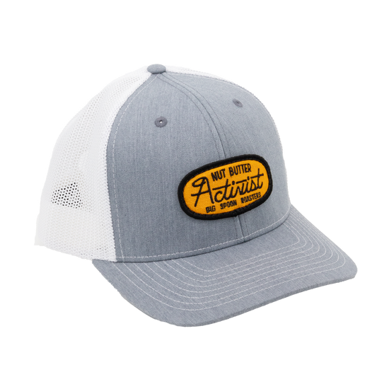 Light gray trucker hat with yellow patch reading "NUT BUTTER ACTIVIST BIG SPOON ROASTERS"