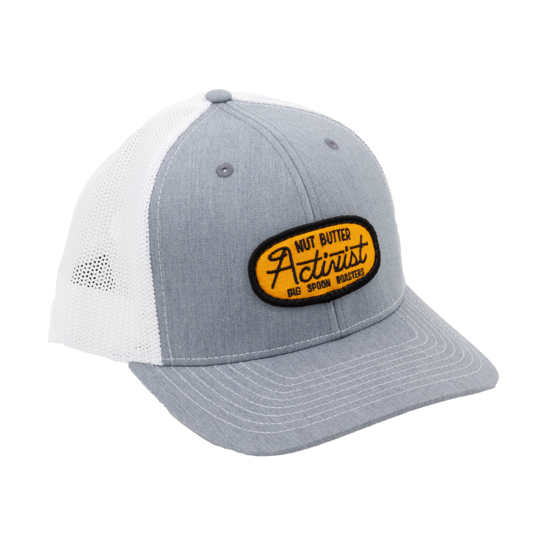 Light gray trucker hat with yellow patch reading "NUT BUTTER ACTIVIST BIG SPOON ROASTERS"